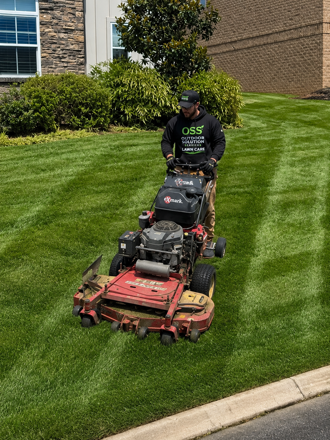 OSS Lawn Care team member operating an eXmark walk-behind mower on a freshly striped commercial lawn
